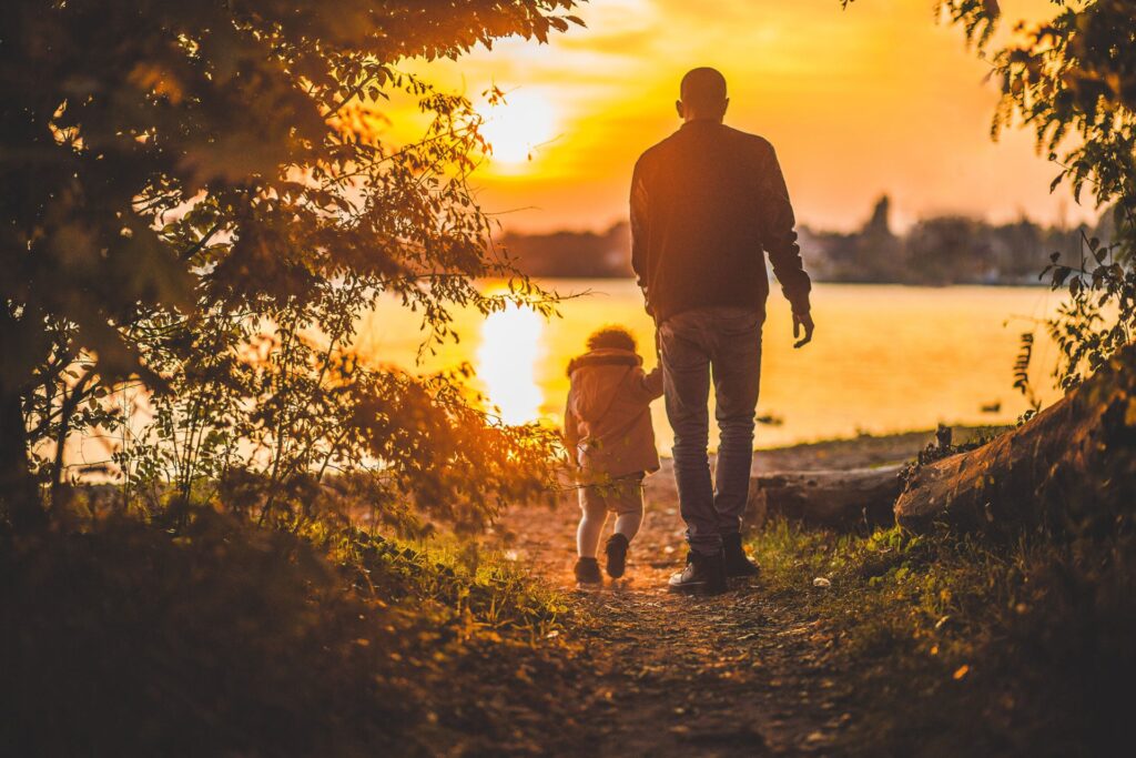 a father and his child walking towards a sunset